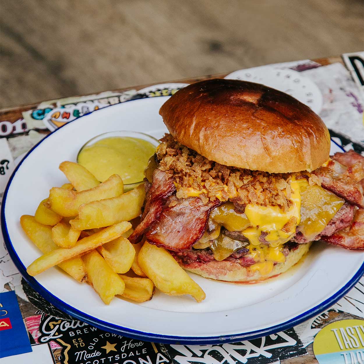 Apetecible Burger Doble Cheddar de la hamburguesería Garua Bar, con carne de chuleta de 360gr, cocinada a la plancha, acompañada por una generosa capa de doble queso cheddar fundido, doble de bacon crujiente, cebolla frita dorada y unas patatas de guarnición en la hamburguesería Garua Bar de Donostia-San Sebastián