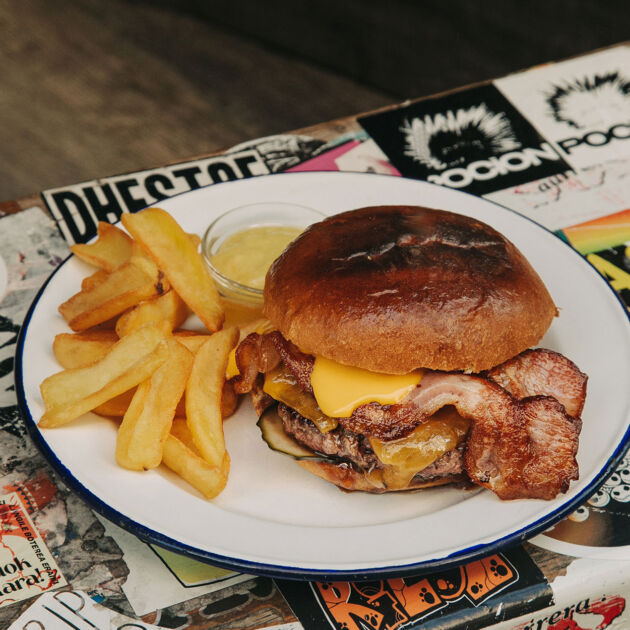 Hamburguesa Cheddar Garua con 180 g de carne de chuleta, queso cheddar a la plancha fundido, pepinillos encurtidos, salsa barbacoa ahumada, bacon crujiente y patatas doradas, en Garua Bar de Donostia-San Sebastián