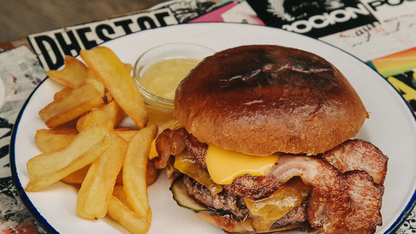 Hamburguesa Cheddar Garua con 180 g de carne de chuleta, queso cheddar a la plancha fundido, pepinillos encurtidos, salsa barbacoa ahumada, bacon crujiente y patatas doradas, en Garua Bar de Donostia-San Sebastián