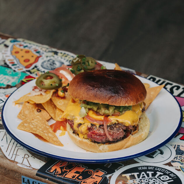 Hamburguesa Mexicana Garúa con 180 g de carne de chuleta, mahonesa de jalapeño, cheddar, guacamole, cilantro, cebolla encurtida, pico de gallo y nachos de guarnición, en Garua Bar de Donostia-San Sebastián