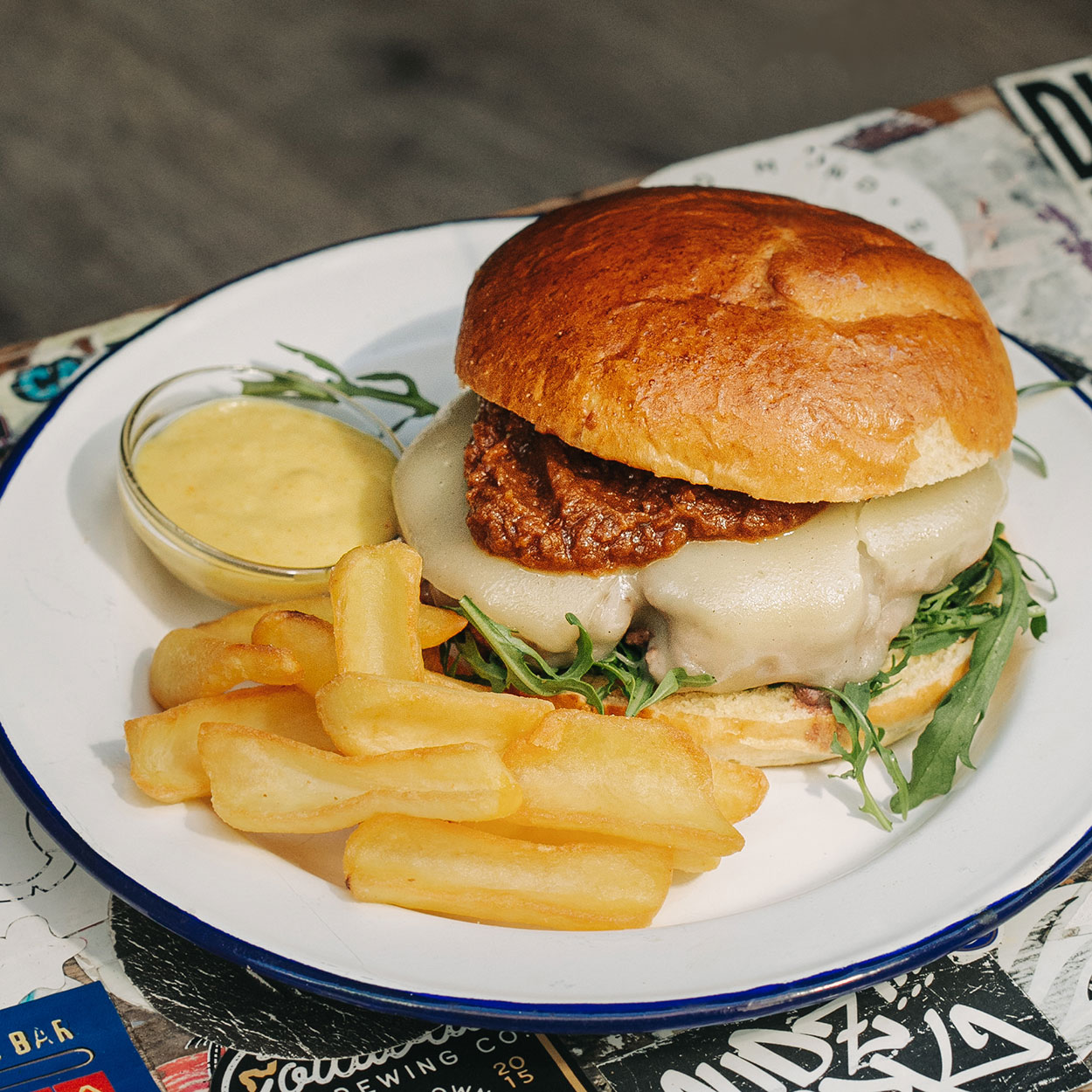 Hamburguesa Provolone Garúa con 180 g de carne de chuleta jugosa, queso provolone fundido, mahonesa con chimichurri, rúcula, tomate seco y patatas crujientes, en Garúa Bar de Donostia-San Sebastián
