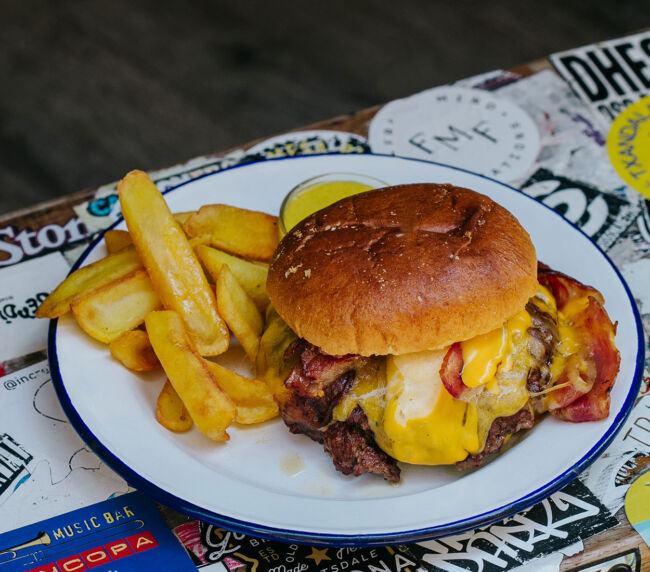 Hamburguesa Smash Garua con 180 g de carne de chuleta en dos discos crujientes, bacon crujiente, cebolla brunoise, queso cheddar fundido, salsa especial Garua y patatas doradas, en Garua Bar de Donostia-San Sebastián