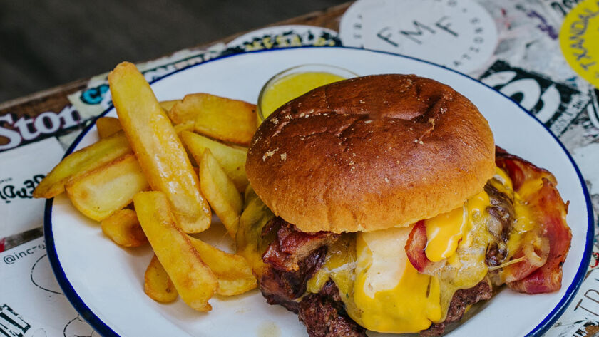 Hamburguesa Smash Garua con 180 g de carne de chuleta en dos discos crujientes, bacon crujiente, cebolla brunoise, queso cheddar fundido, salsa especial Garua y patatas doradas, en Garua Bar de Donostia-San Sebastián
